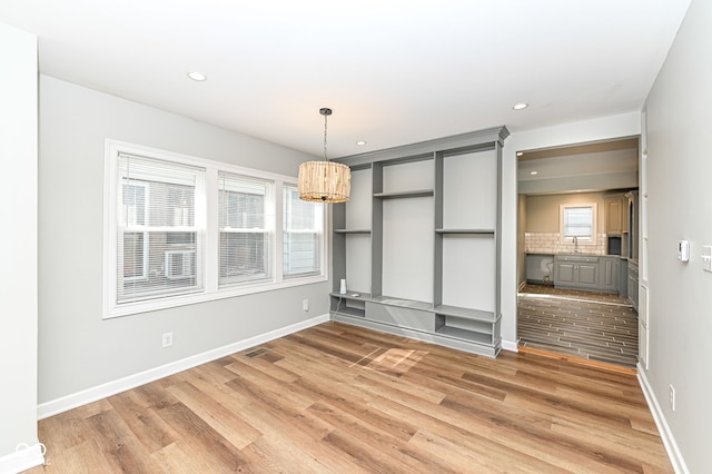 unfurnished dining area with a sink, baseboards, plenty of natural light, and light wood-style floors