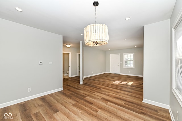 empty room featuring recessed lighting, wood finished floors, baseboards, and a chandelier