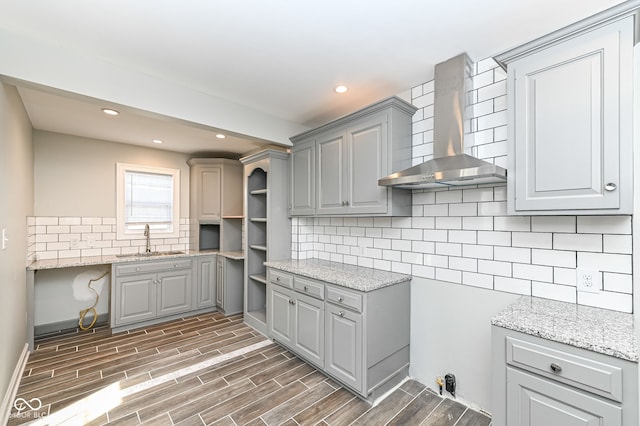 kitchen featuring gray cabinets, a sink, tasteful backsplash, wall chimney exhaust hood, and wood tiled floor