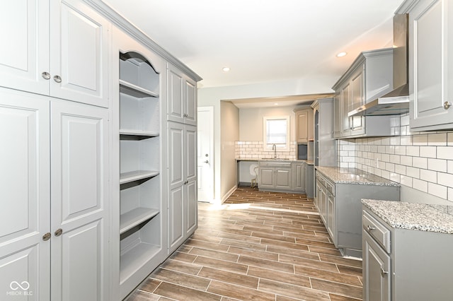 kitchen with wood finish floors, gray cabinets, wall chimney range hood, and decorative backsplash