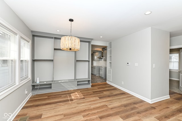 unfurnished dining area with recessed lighting, a notable chandelier, baseboards, and light wood-style floors