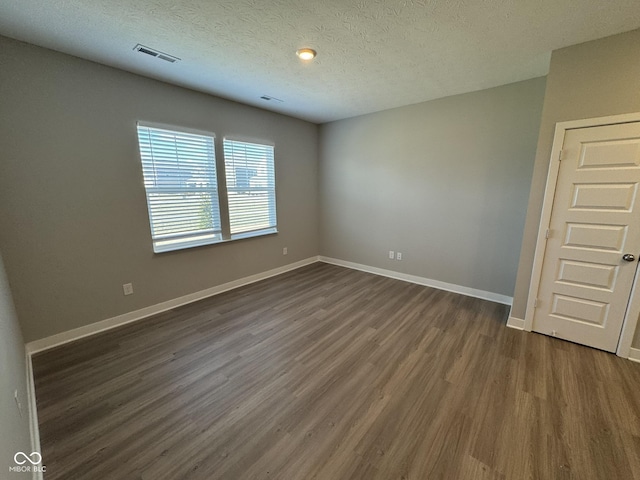 unfurnished room with visible vents, dark wood finished floors, a textured ceiling, and baseboards