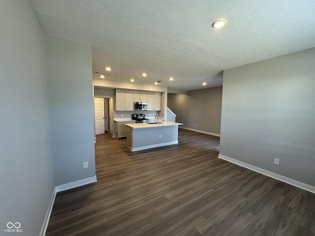 kitchen featuring dark wood-style flooring, a center island with sink, stainless steel appliances, light countertops, and baseboards