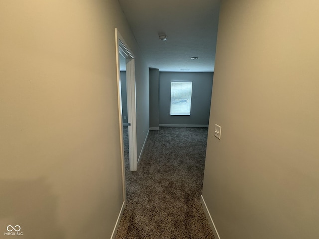 corridor with baseboards and dark carpet