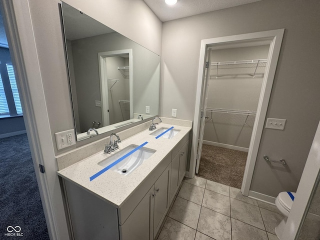 bathroom featuring double vanity, a spacious closet, a sink, and toilet