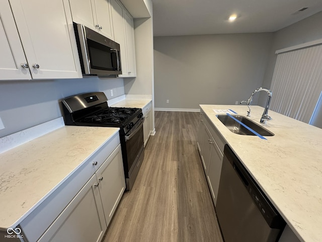 kitchen with visible vents, appliances with stainless steel finishes, light stone counters, wood finished floors, and a sink