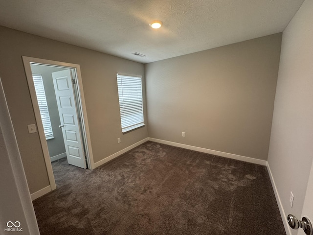 empty room featuring a textured ceiling, dark carpet, visible vents, and baseboards