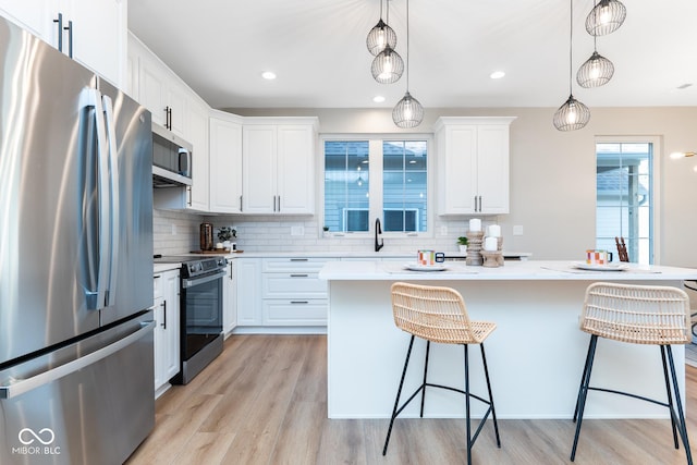 kitchen featuring appliances with stainless steel finishes, white cabinetry, light wood finished floors, and a kitchen breakfast bar