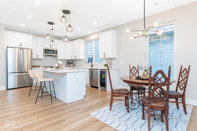 kitchen with white cabinets, appliances with stainless steel finishes, backsplash, a center island, and light wood finished floors