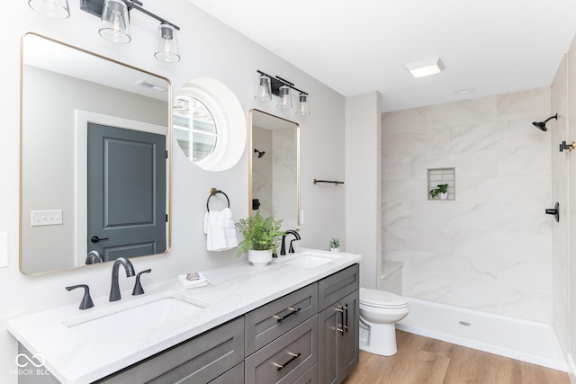 bathroom featuring wood finished floors, tiled shower, a sink, and toilet