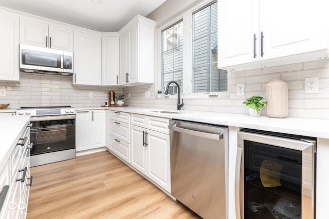 kitchen featuring wine cooler, stainless steel appliances, white cabinetry, a sink, and light wood-type flooring