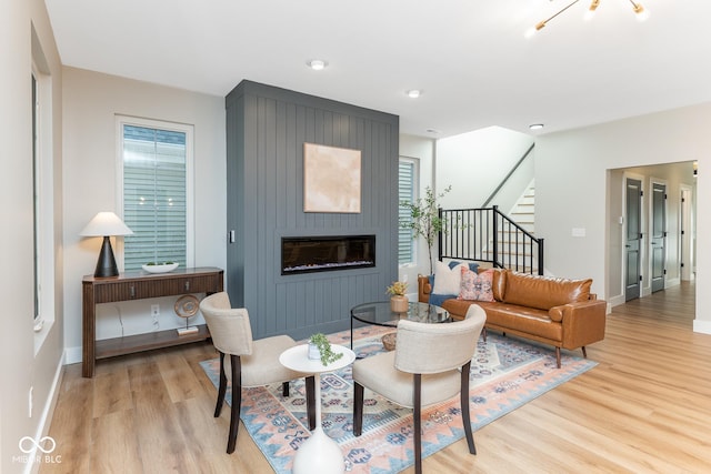 living area featuring light wood-style flooring, stairs, baseboards, and a fireplace