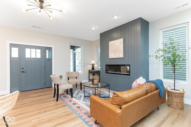 living area featuring a large fireplace, light wood-style flooring, visible vents, and an inviting chandelier