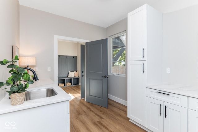 interior space featuring light stone counters, white cabinets, a sink, light wood-type flooring, and baseboards