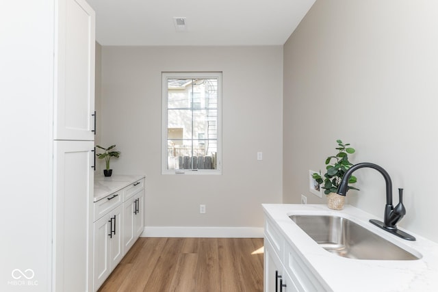 kitchen with baseboards, a sink, light wood-style flooring, and white cabinetry