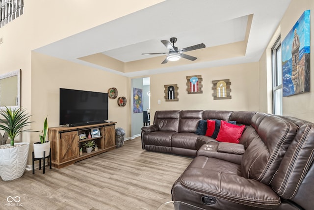 living room featuring baseboards, ceiling fan, a tray ceiling, and wood finished floors