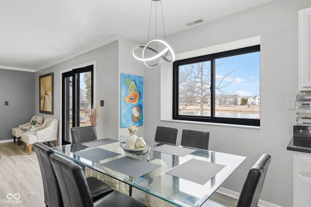 dining space with light wood finished floors, visible vents, baseboards, an inviting chandelier, and crown molding