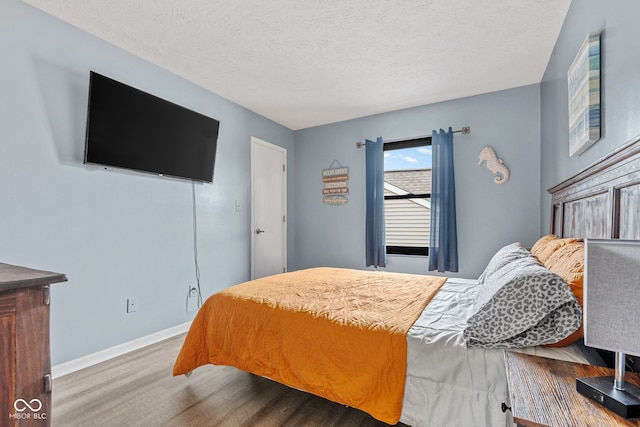 bedroom featuring a textured ceiling, baseboards, and wood finished floors