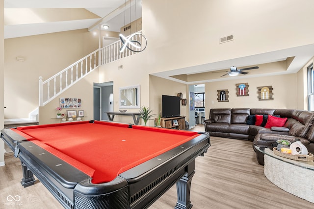 game room with a tray ceiling, light wood finished floors, visible vents, a towering ceiling, and a ceiling fan