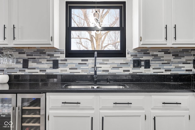 kitchen featuring beverage cooler, tasteful backsplash, a sink, and white cabinetry