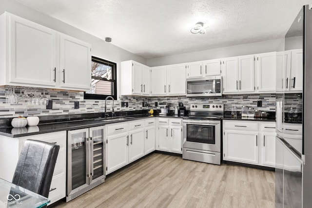 kitchen featuring wine cooler, appliances with stainless steel finishes, light wood-style floors, white cabinets, and a sink