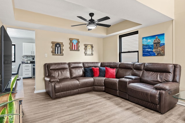 living area featuring ceiling fan, a tray ceiling, baseboards, and light wood-style floors