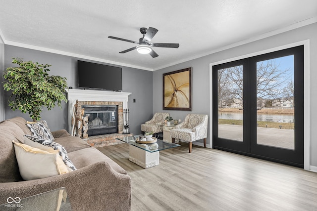 living area featuring light wood-style flooring, ornamental molding, a textured ceiling, french doors, and a brick fireplace