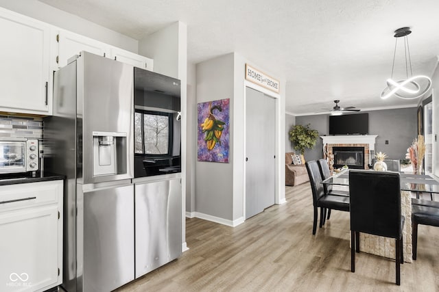 kitchen with backsplash, light wood-style floors, a brick fireplace, white cabinetry, and stainless steel fridge