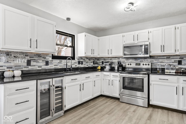 kitchen with wine cooler, a sink, white cabinetry, light wood-style floors, and appliances with stainless steel finishes