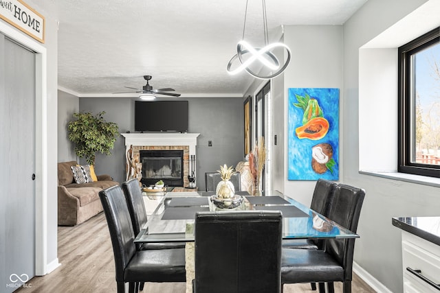 dining space featuring a brick fireplace, ceiling fan, baseboards, and wood finished floors