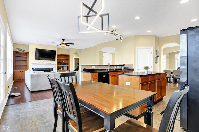 dining area featuring a ceiling fan, arched walkways, a healthy amount of sunlight, and a fireplace