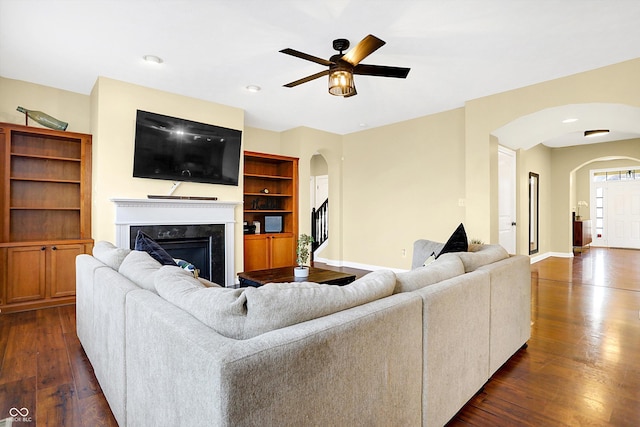 living room featuring arched walkways, dark wood-style flooring, a premium fireplace, and baseboards