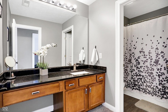 bathroom with a shower with shower curtain, wood finished floors, vanity, visible vents, and baseboards