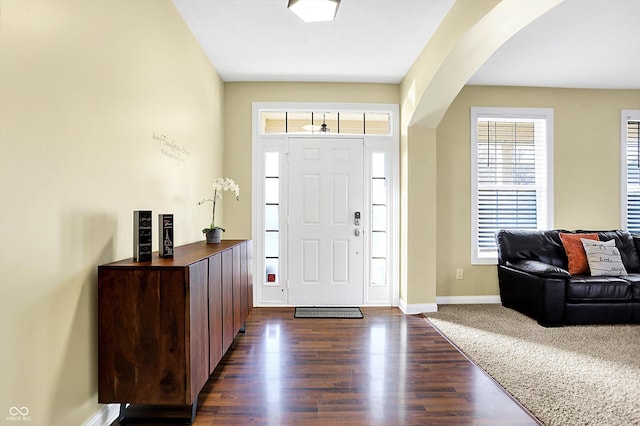 foyer with arched walkways, dark wood finished floors, and baseboards