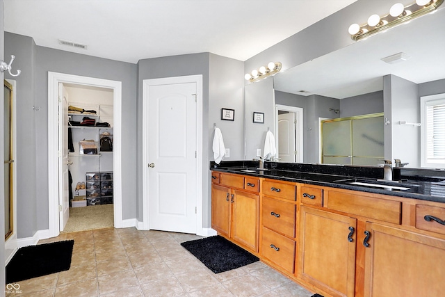 full bath featuring a stall shower, visible vents, a sink, and double vanity