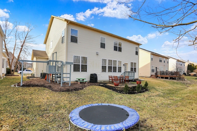 rear view of property with a trampoline, cooling unit, a yard, and a wooden deck