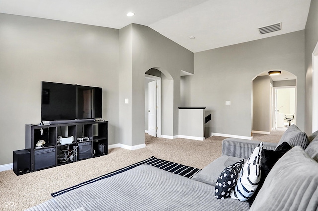 carpeted living area with arched walkways, vaulted ceiling, visible vents, and baseboards