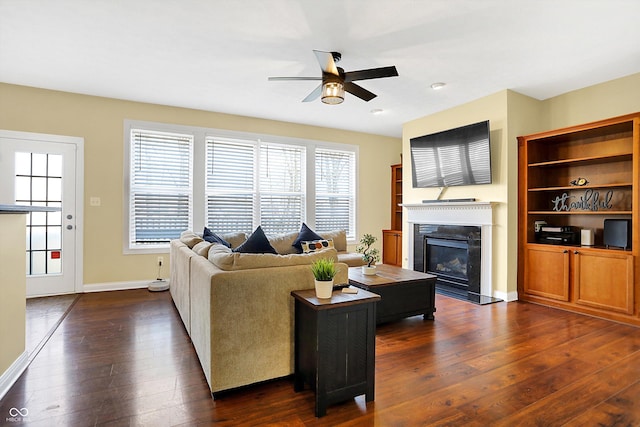 living room with ceiling fan, a fireplace, baseboards, and dark wood-style flooring