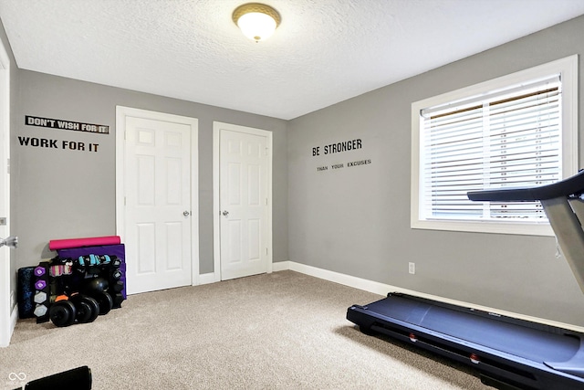 exercise room featuring a textured ceiling, baseboards, and carpet flooring