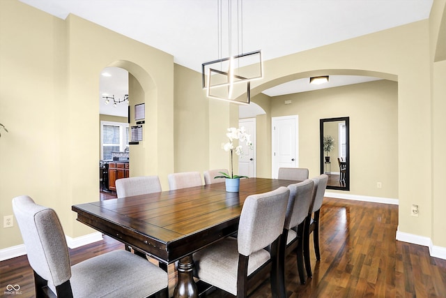 dining room with baseboards, arched walkways, and dark wood finished floors