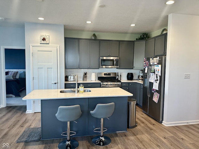 kitchen with light wood finished floors, a breakfast bar area, stainless steel appliances, tasteful backsplash, and a sink