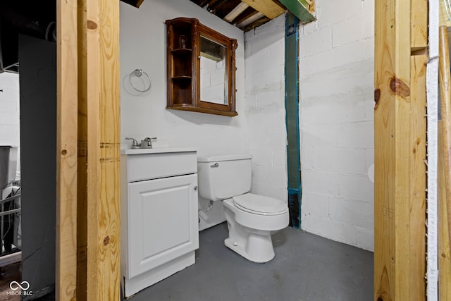 bathroom featuring toilet, concrete block wall, concrete floors, and vanity