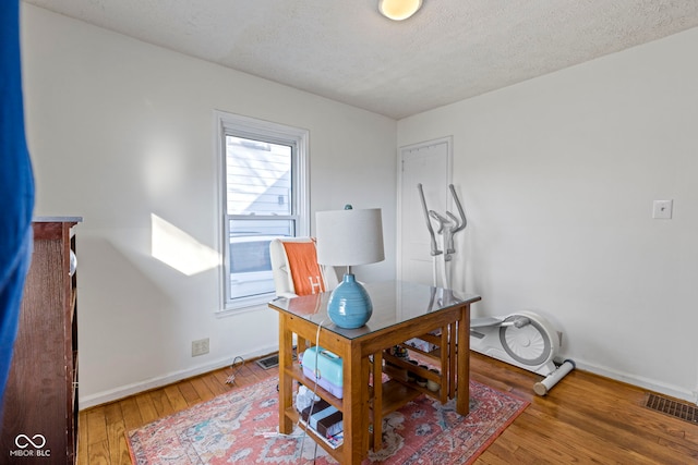 office space featuring baseboards, a textured ceiling, visible vents, and hardwood / wood-style floors