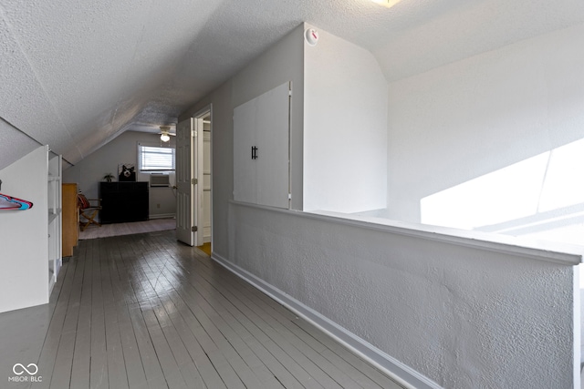 additional living space featuring baseboards, a textured wall, lofted ceiling, hardwood / wood-style flooring, and a textured ceiling