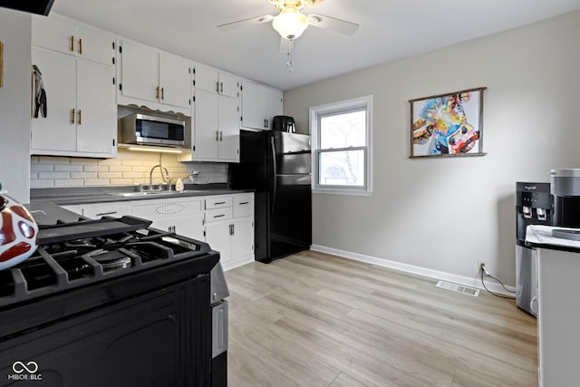 kitchen featuring dark countertops, light wood-style flooring, backsplash, a sink, and black appliances