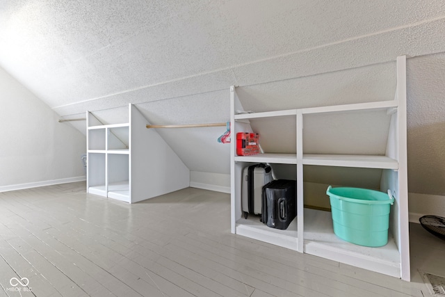 additional living space with a textured ceiling, baseboards, vaulted ceiling, and wood finished floors