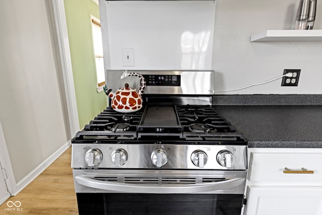 kitchen featuring baseboards, stainless steel gas stove, light wood finished floors, and white cabinetry