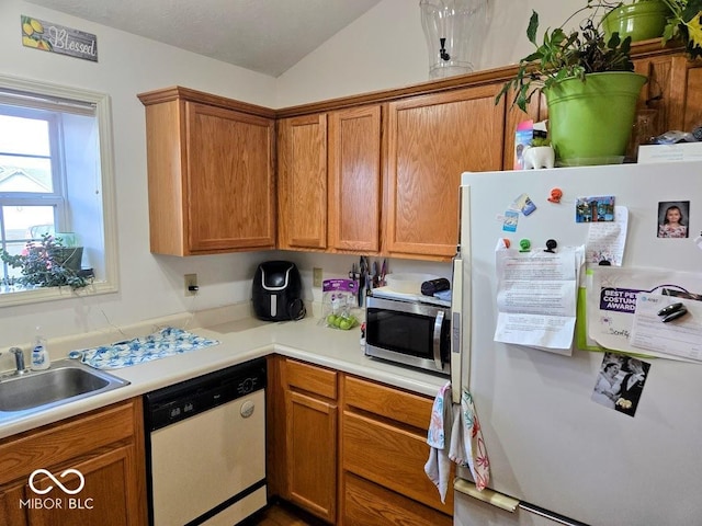 kitchen with white appliances, brown cabinetry, vaulted ceiling, light countertops, and a sink