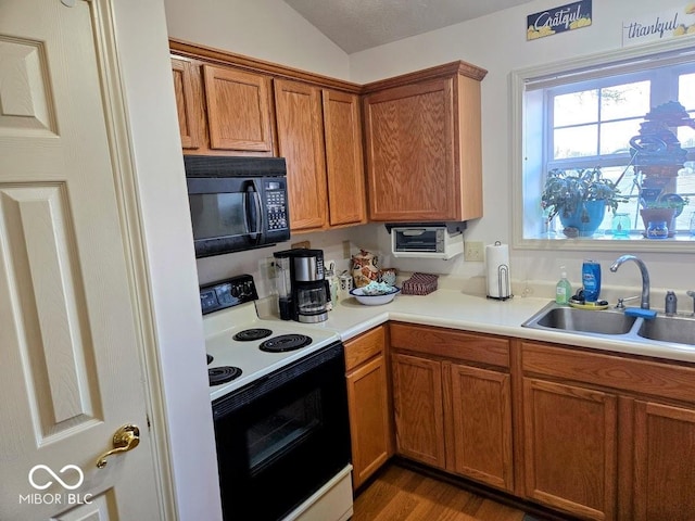 kitchen featuring black microwave, range with electric stovetop, a sink, light countertops, and brown cabinets