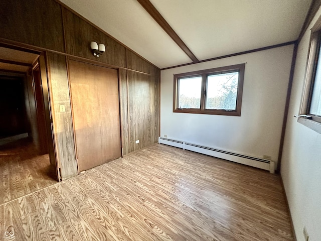 unfurnished bedroom with a closet, wood finished floors, a baseboard heating unit, and vaulted ceiling